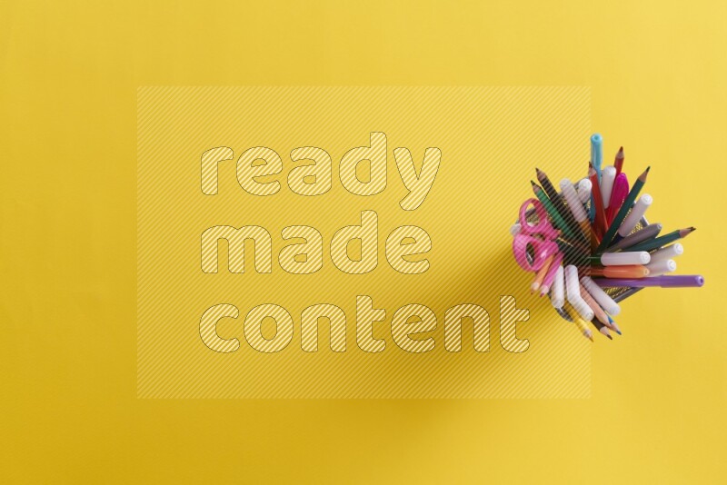 Pens, pencils and school supplies in a metal pen holder on yellow background
