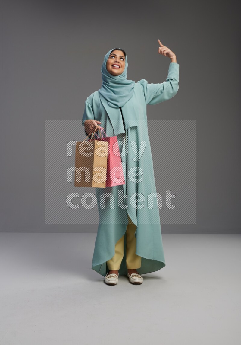 Saudi Woman wearing Abaya standing holding shopping bag on Gray background