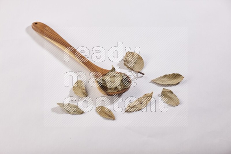 A wooden ladle filled with dried bay leaves on white flooring in different angles