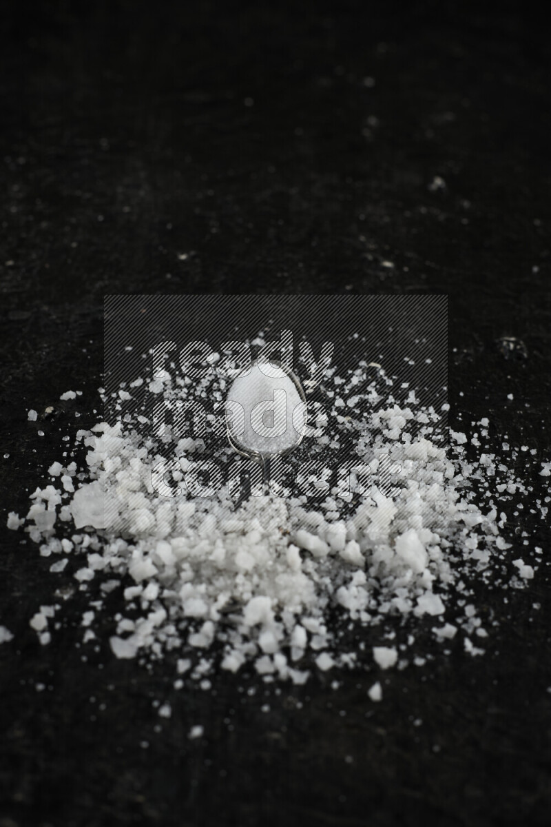 ملعقتان معدنيتان ممتلئتان بالملح الأبيض على خلفية سوداء