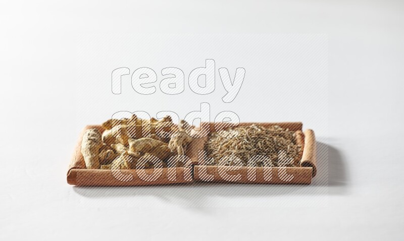 مربعان من أعواد القرفة ممتلئان بحبوب الكمون وأصابع الكركم علي خلفية بيضاء