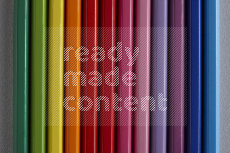 A collection of colored pencils arranged showcasing a gradient of different hues on grey background