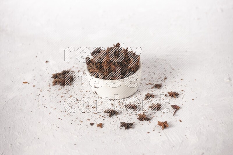 Star Anise in a white bowl and more of it sprinkled on white background