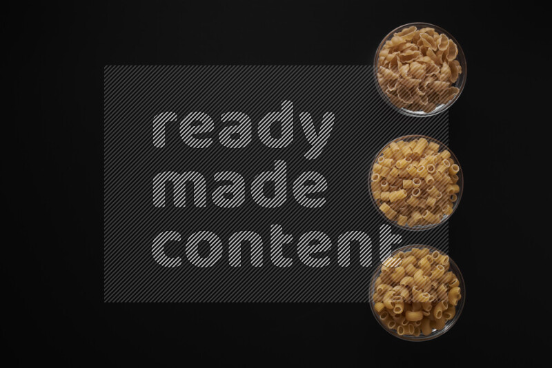Different pasta types in 3 glass bowls on black background