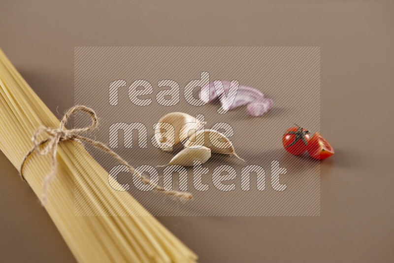 Raw pasta with different ingredients such as cherry tomatoes, garlic, onions, red chilis, black pepper, white pepper, bay laurel leaves, rosemary and cardamom on beige background