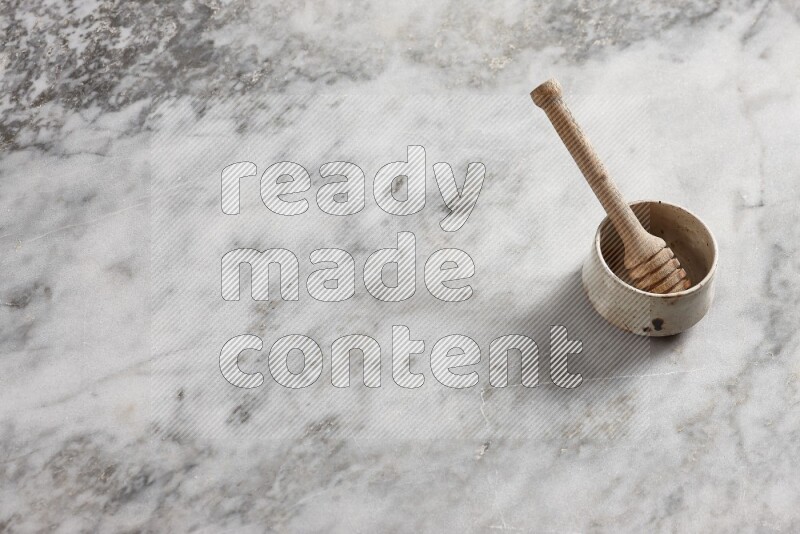 Beige pottery bowl with wooden honey dipper in it on grey marble background