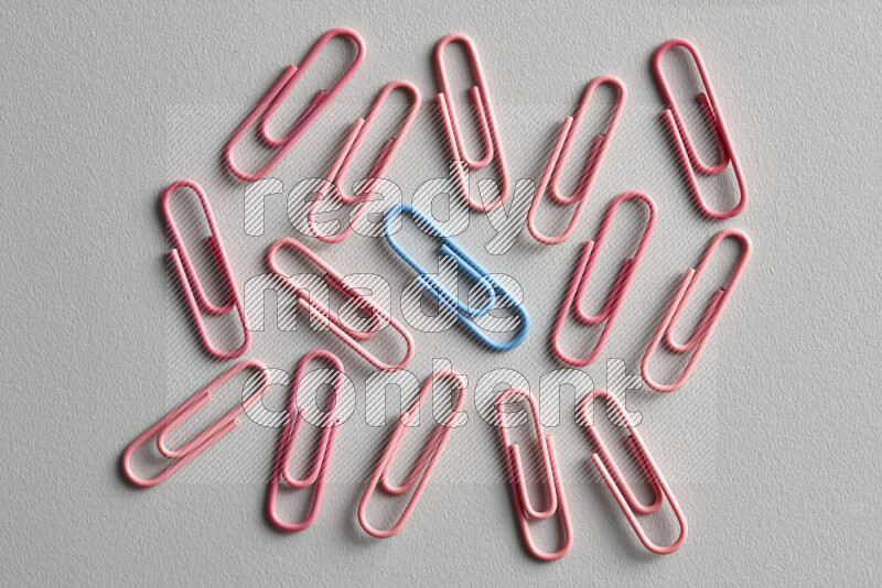 A bunch of pink paper clips with a different colored paper clip in the center on grey background