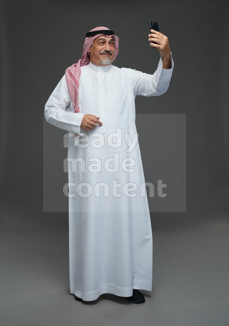 Saudi man with shomag Standing taking selfie on gray background