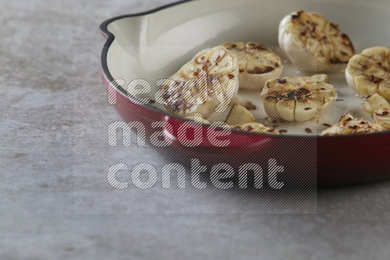 half's roasted garlic in a red-coated cast iron pan on a grey textured countertop