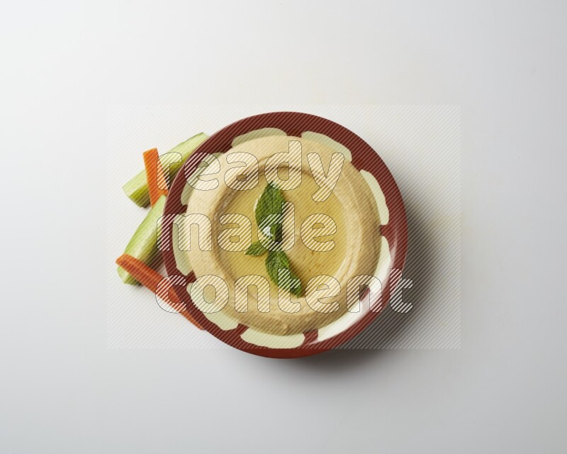 Hummus in a traditional plate garnished with mint on a white background