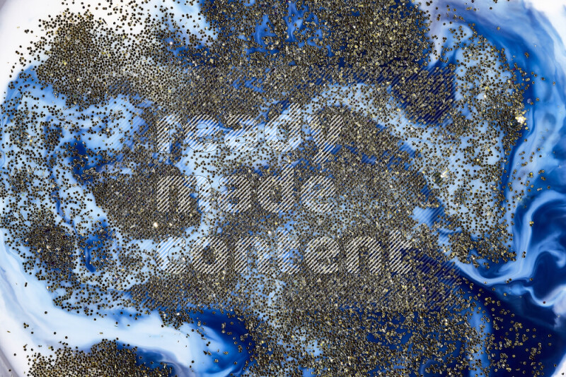 A close-up of sparkling gold glitter scattered on swirling blue background