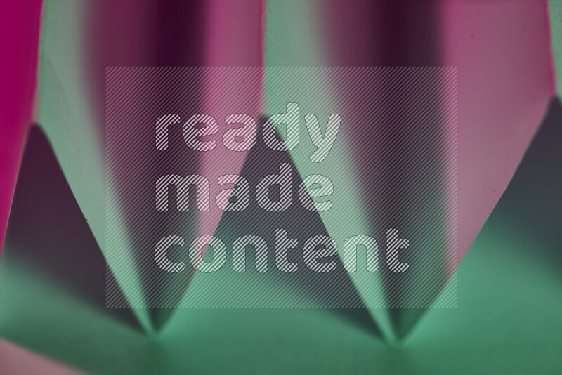 A close-up abstract image showing sharp geometric paper folds in green and pink gradients