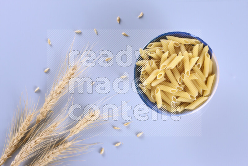 Raw pasta with wheat stalks on light blue background