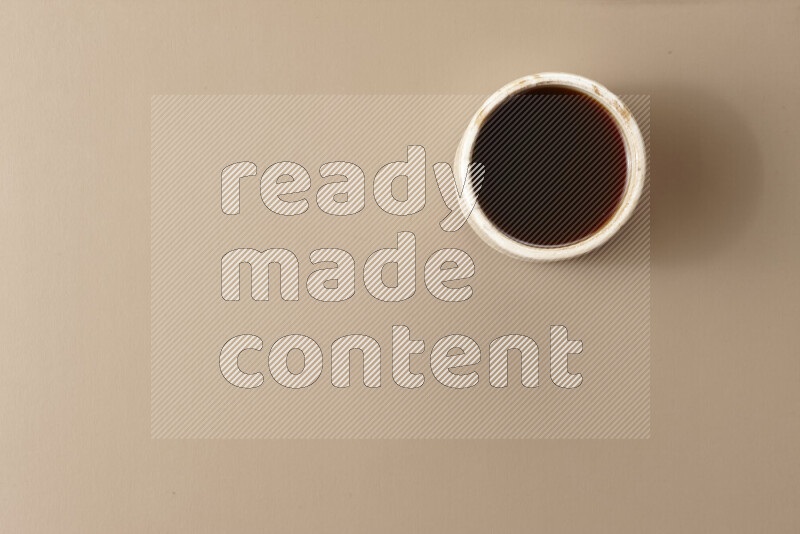 A beige pottery cup of coffee surrounded by roasted coffee beans on beige background