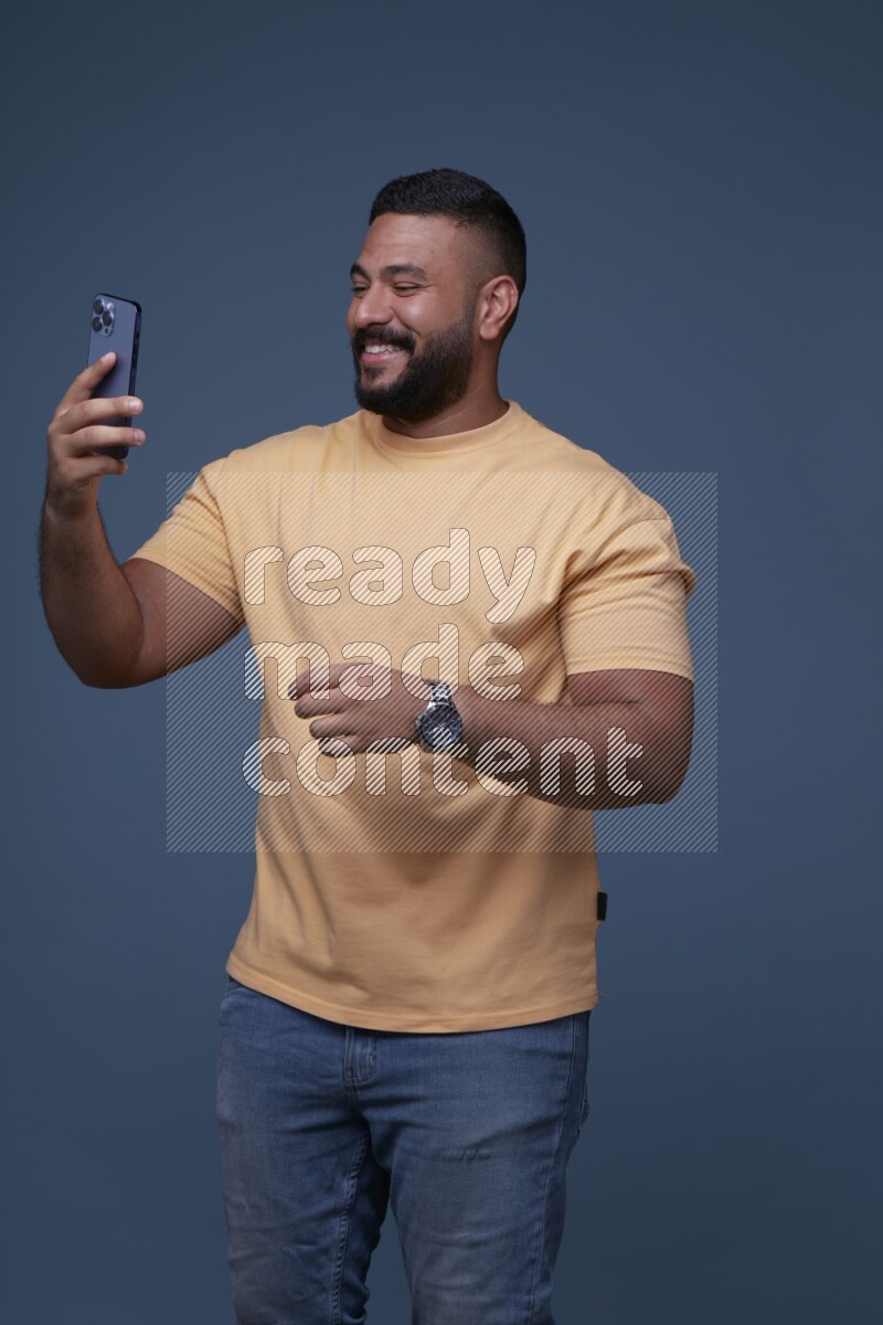 A man Texting on his phone on Blue Background wearing Orange T-shirt