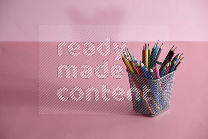 Pens, pencils and other different school supplies in a metal pen holder on rose background