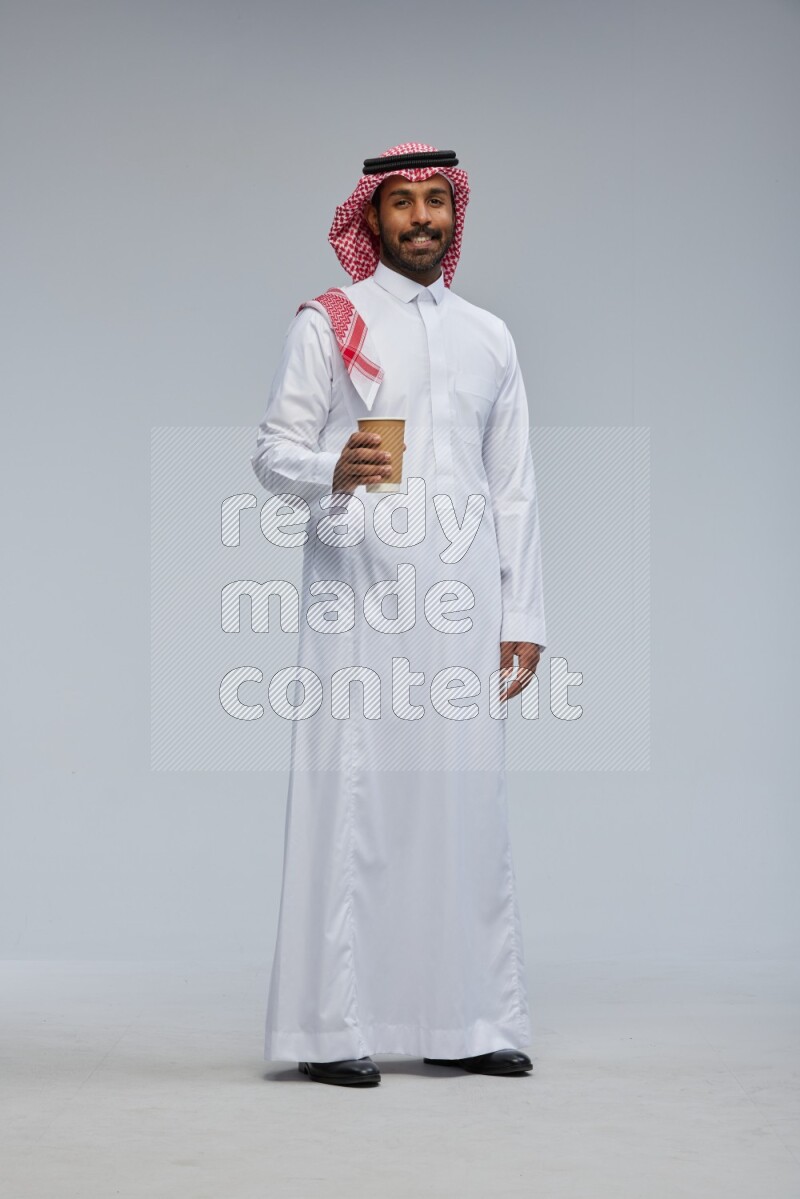 Saudi man Wearing Thob and shomag standing holding paper cup on Gray background