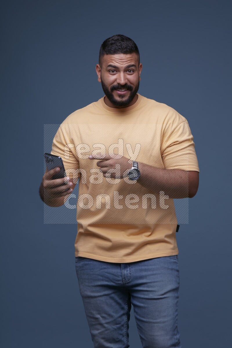 A man Pointing at a Smartphone on Blue Background wearing Orange T-shirt