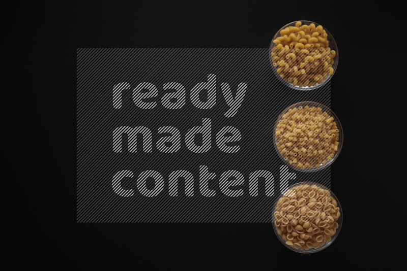 Different pasta types in 3 glass bowls on black background