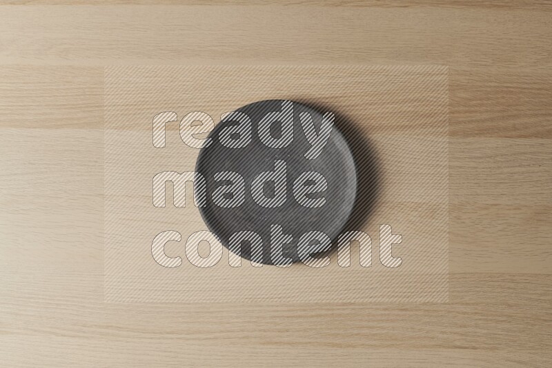 A circular black pottery plate on light wooden background