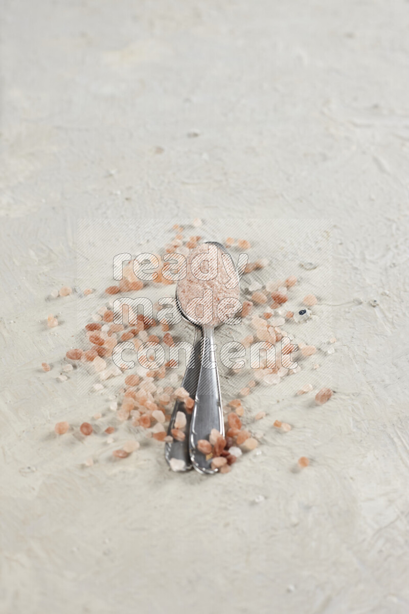 2 metal spoons filled with fine table salt and fine pink himalayan salt on white background