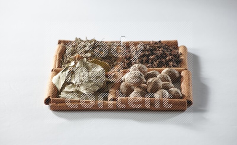4 squares of cinnamon sticks full of bay laurel leaves, dried basil, cloves and nutmegs on white flooring
