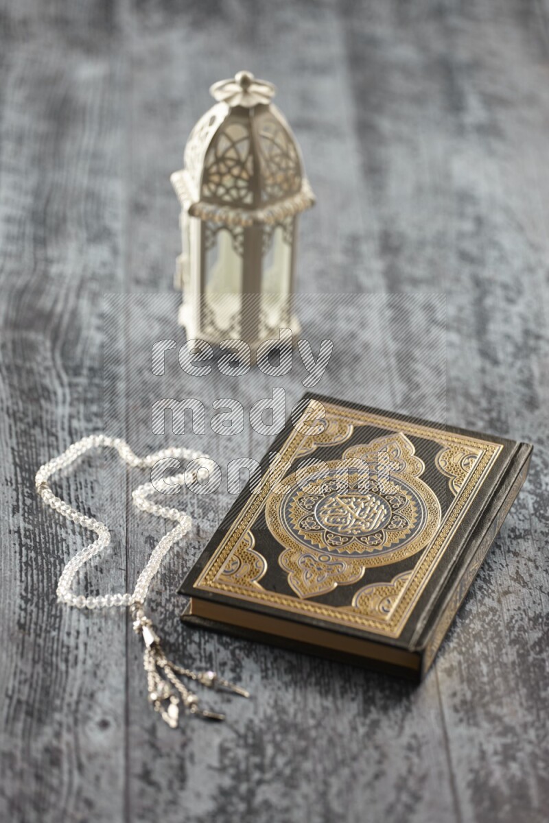A white lantern with different drinks, dates, nuts, prayer beads and quran on grey wooden background