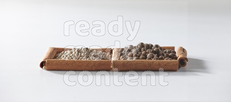 مربعان من أعواد القرفة ممتلئان بحبوب الفلفل الأبيض وحبوب الفلفل الحلو علي خلفية بيضاء