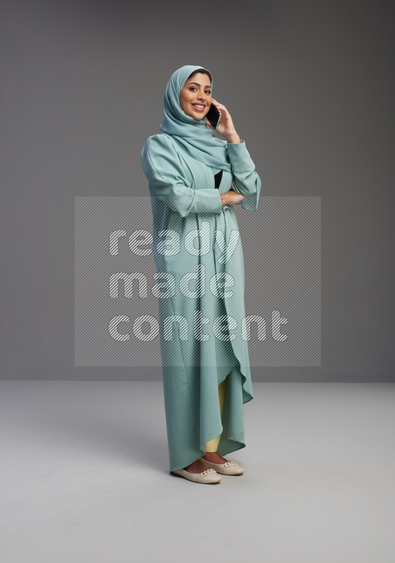 Saudi Woman wearing Abaya standing talking on phone on Gray background