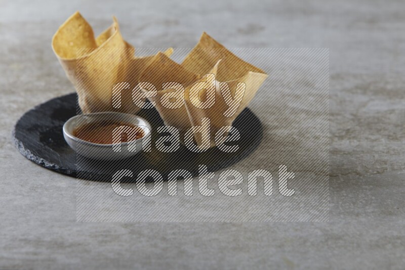 wonton cups with soy sauce ramkin on circle slate on grey textured counter top