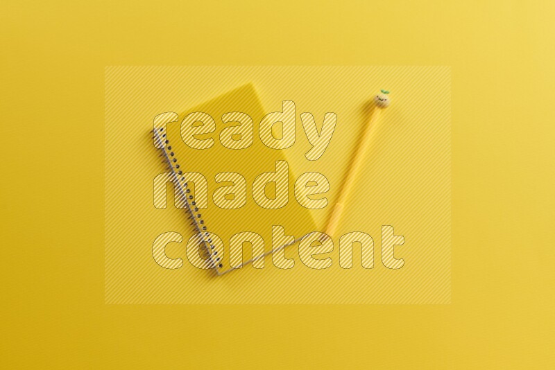 A yellow notebook with different school supplies on yellow background