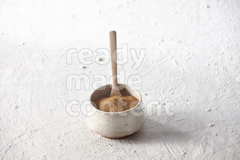 Ceramic beige bowl full of cinnamon powder with a wooden spoon on a textured white background