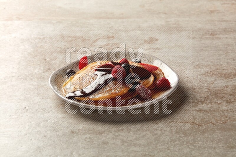 Three stacked mixed berries pancakes in an irregular plate on beige background