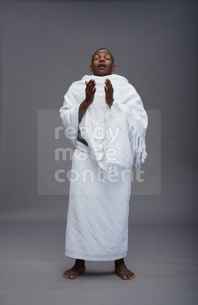 A man wearing Ehram standing showing how to sneeze on gray background