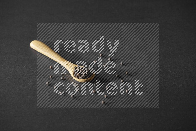 A wooden spoon full of black pepper on a black flooring