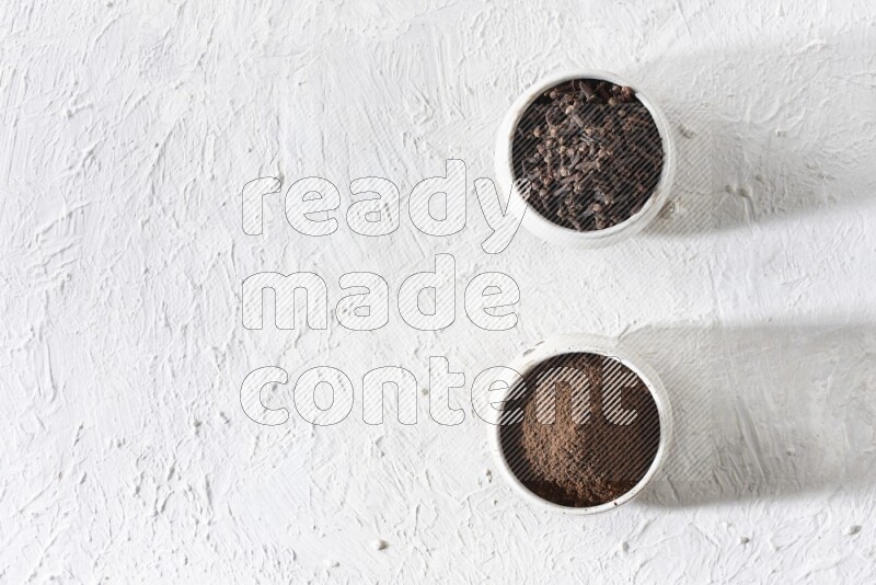2 Beige ceramic bowls, one full of cloves and the other full of powder on textured white flooring