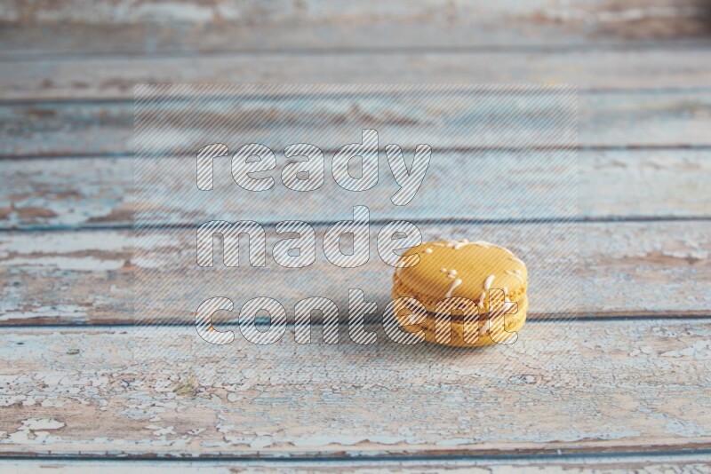 45º Shot of Yellow Piña Colada macaron on light blue wooden background