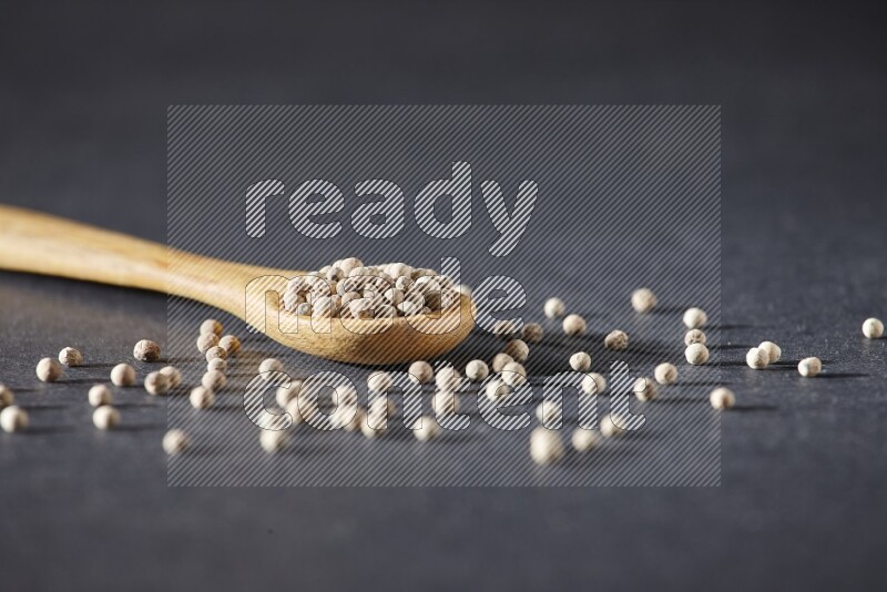 A wooden spoon full of white pepper beads on black flooring