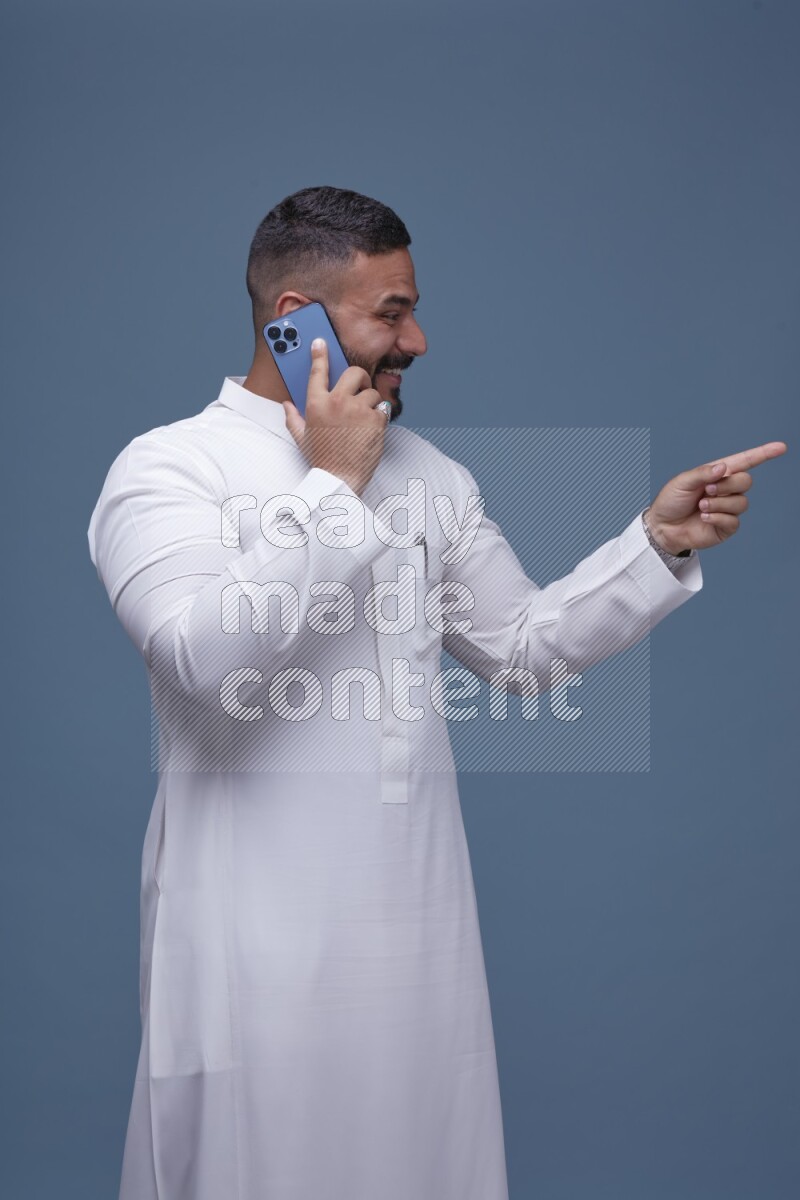 A Saudi man calling on blue background wearing Saudi Thob