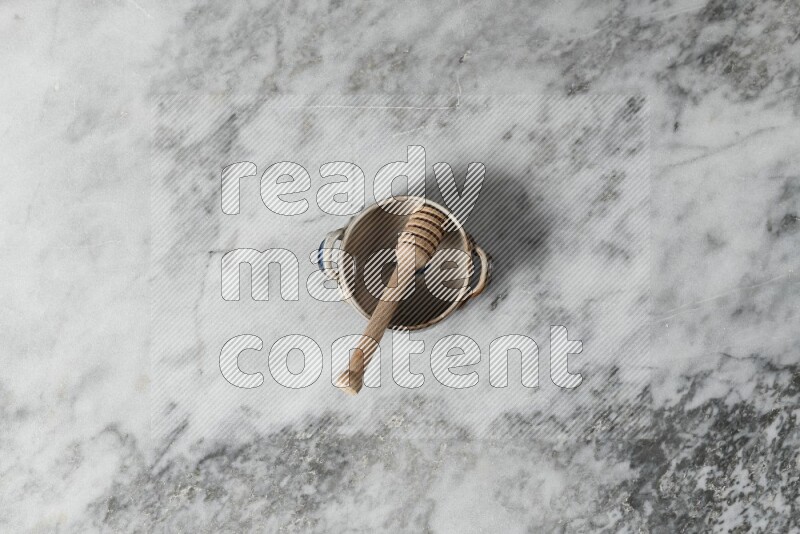 Multicolored pottery bowl with wooden honey dipper in it on grey marble background