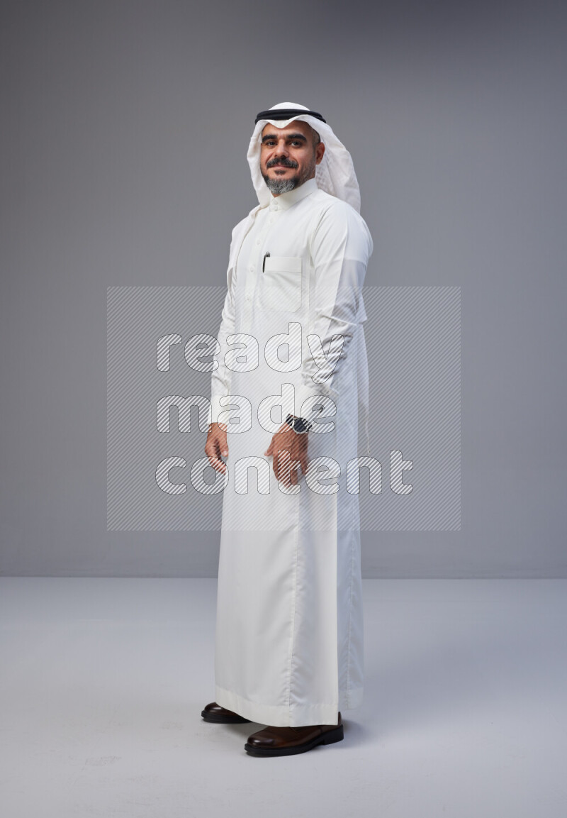 Saudi man Wearing Thob and white Shomag standing interacting with the camera on Gray background