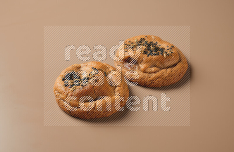 Two chocolate chip cookies on a brown background