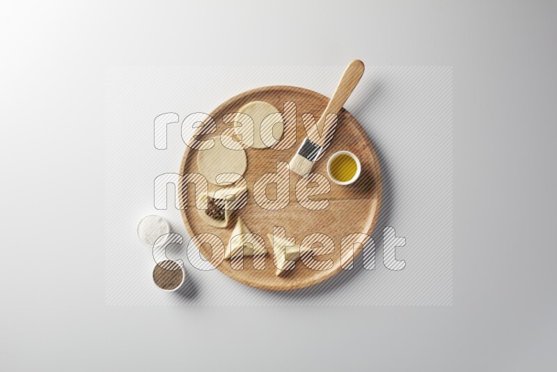 two closed sambosas and one open sambosa filled with meat while salt, black pepper and oil with oil brush aside in a wooden dish on a white background