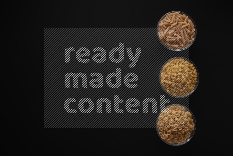 Different pasta types in 3 glass bowls on black background