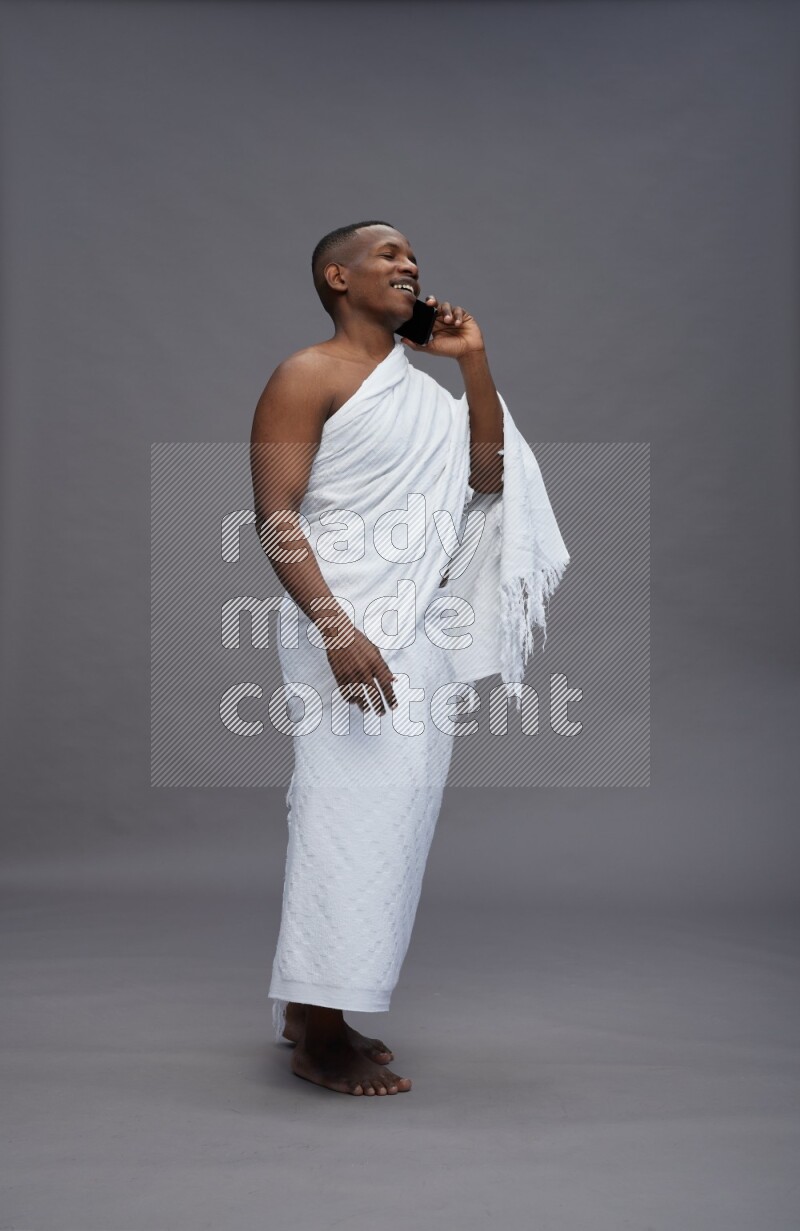 A man wearing Ehram Standing talking on phone on gray background