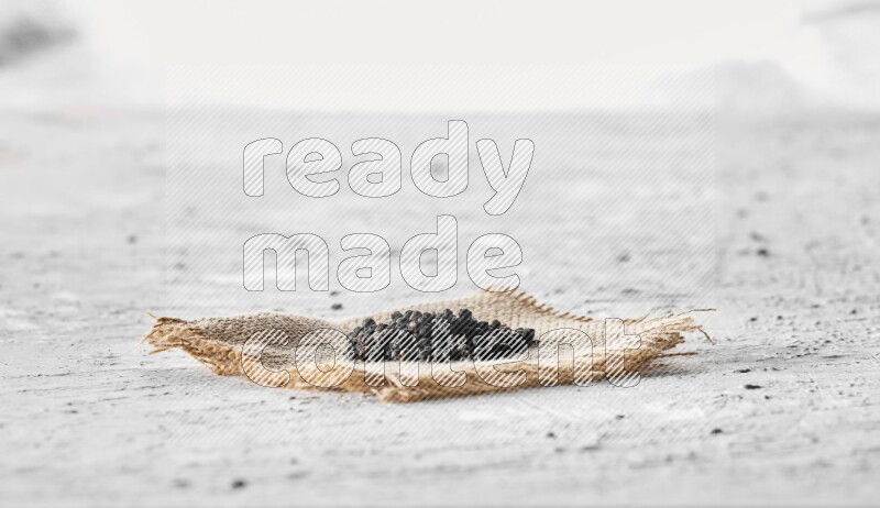 Black pepper on burlap fabric on a textured white flooring