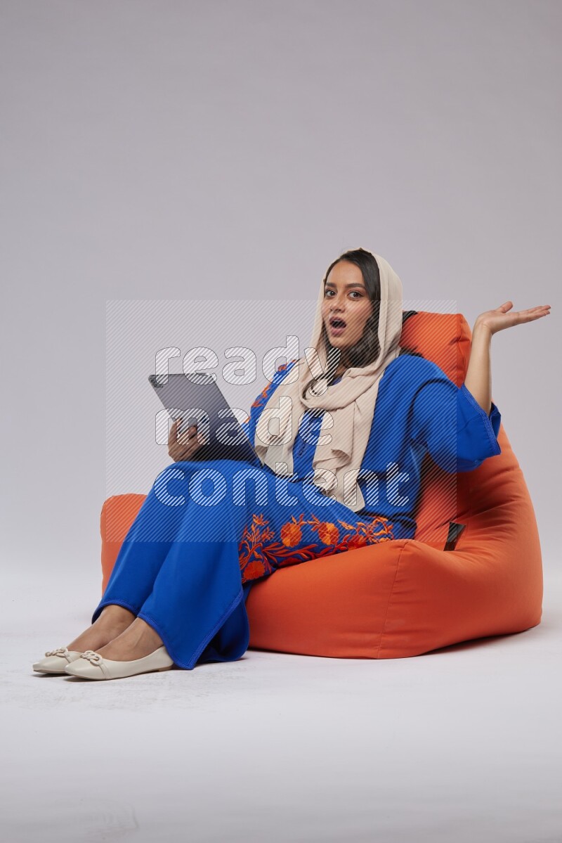 A Saudi woman sitting on an orange beanbag and working on tablet