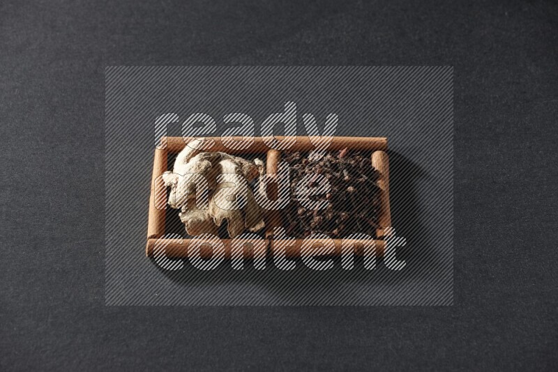 مربعان من أعواد القرفة ممتلئان بالقرنفل والزنجبيل المجفف علي خلفية سوداء