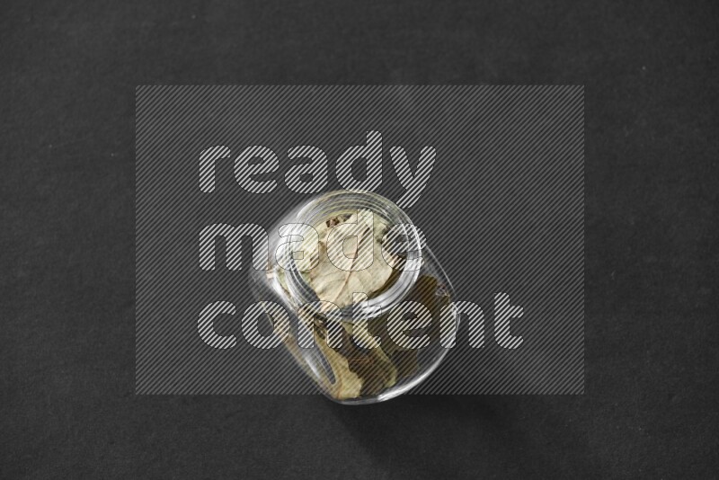 A glass spice jar full of bay laurel leaves on black flooring