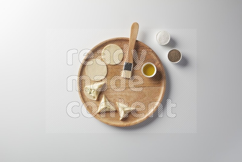 two closed sambosas and one open sambosa filled with cheese while salt, black pepper and oil with oil brush aside in a wooden dish on a white background